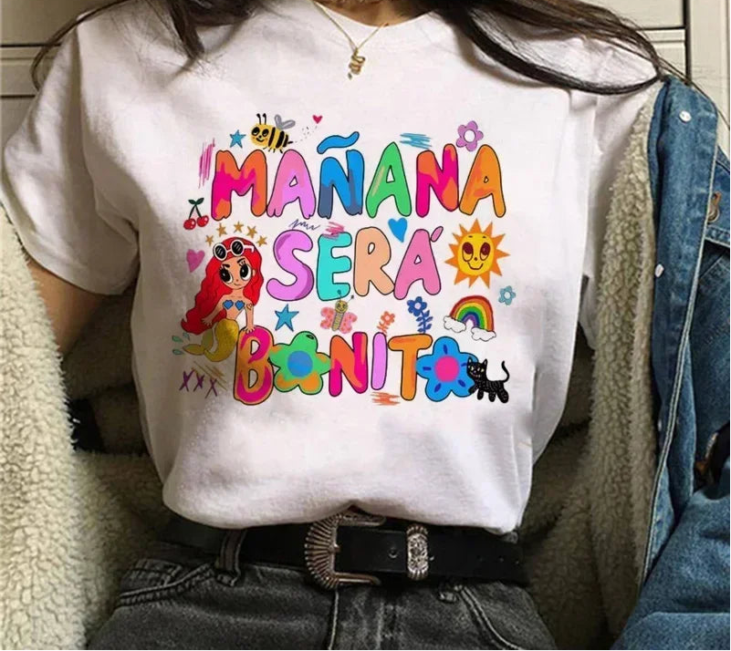 Person wearing a white t-shirt with colorful text and graphics, sitting indoors.