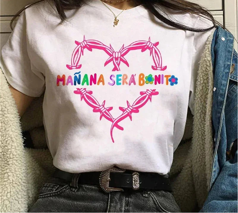 Person wearing a white t-shirt with colorful text and designs, sitting indoors.